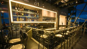 A bar area with a stone wall, multiple shelves of bottles, and several bar stools. - Hotel Labuan Point (Labuan)