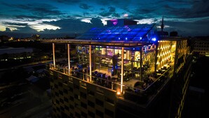 Un edificio moderno con fachada de vidrio, varios niveles y una terraza en la azotea.