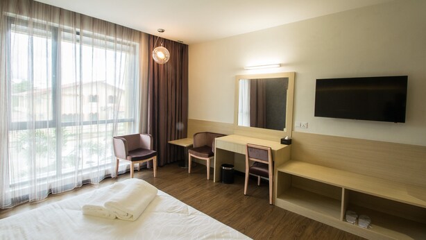 Habitación de hotel con cama, escritorio, silla, televisor y ventana grande con cortinas.