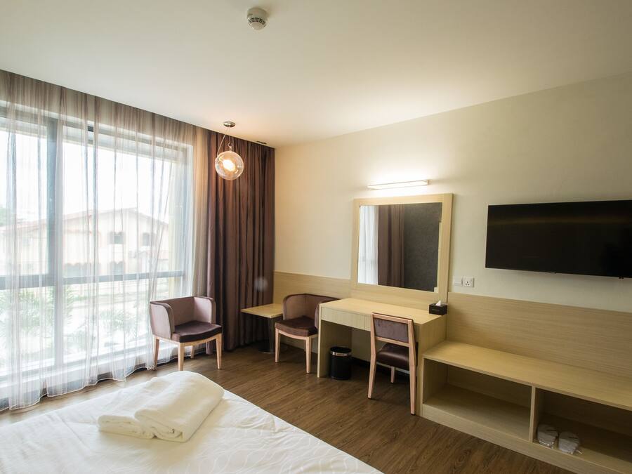 Habitación de hotel con cama, escritorio, silla, televisor y ventana grande con cortinas.