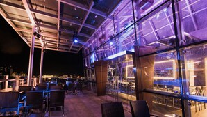 An outdoor seating area with tables and chairs, a glass enclosure, and a view of the cityscape at night. - Hotel Labuan Point (Labuan)