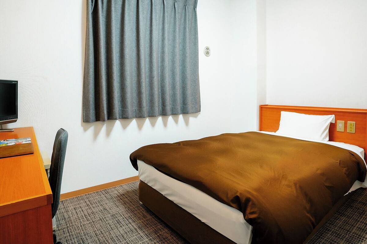 Una habitación de hotel con una cama, un escritorio con ordenador y una ventana con cortinas.