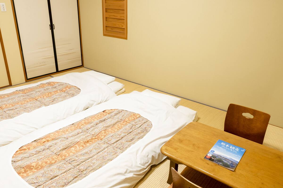 Habitación de hotel con dos camas, una mesa de madera y una silla. Hay un libro sobre la mesa.