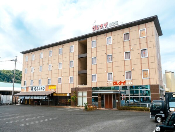 A multi-story hotel with a central entrance, several windows, and a parking lot in front.