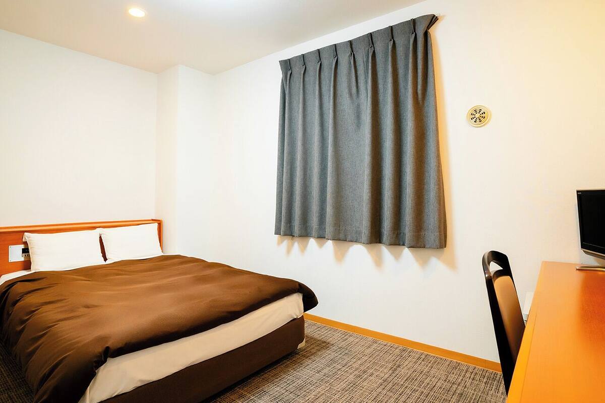 Una habitación de hotel con cama, escritorio y ventana con cortinas.