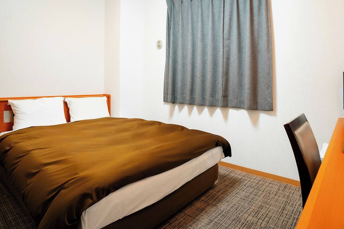 Una habitación de hotel con cama, escritorio y ventana con cortinas.