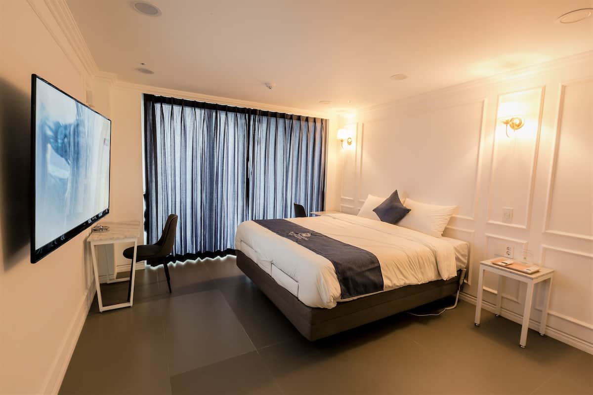 A modern hotel room with a large bed, a desk, a chair, and a TV mounted on the wall.