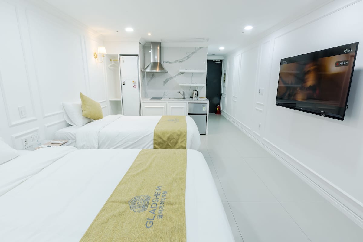 A hotel room with two beds, a kitchenette, a TV, and a bathroom.