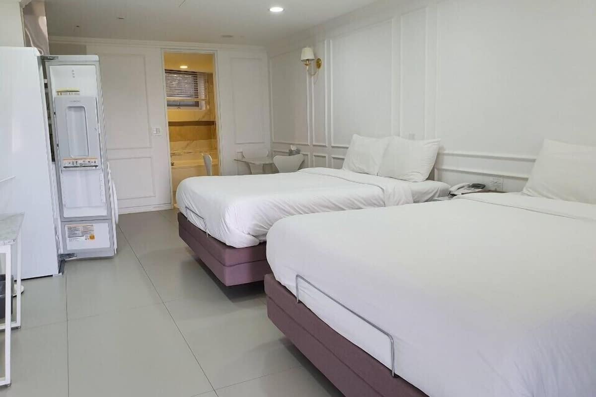 A hotel room with two beds, a desk, a chair, a wardrobe, and a bathroom visible through an open door.