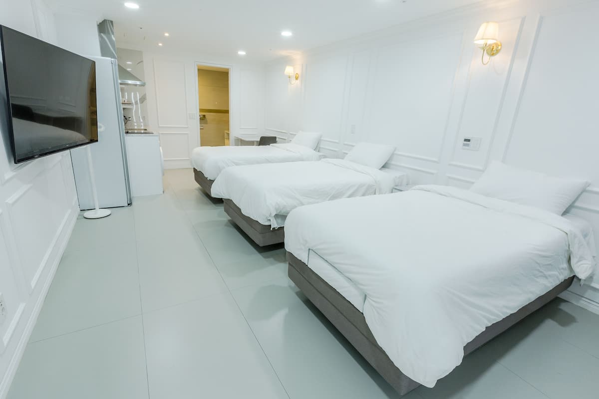 A hotel room with two beds, a TV, a kitchenette, and a bathroom.