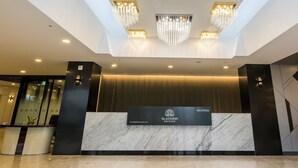A hotel reception area with a marble reception desk, chandeliers, and a modern geometric wall design.