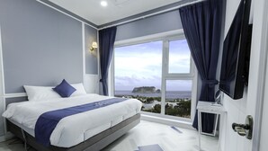 A modern hotel room with a large bed, a view of the sea, and a small table by the window.