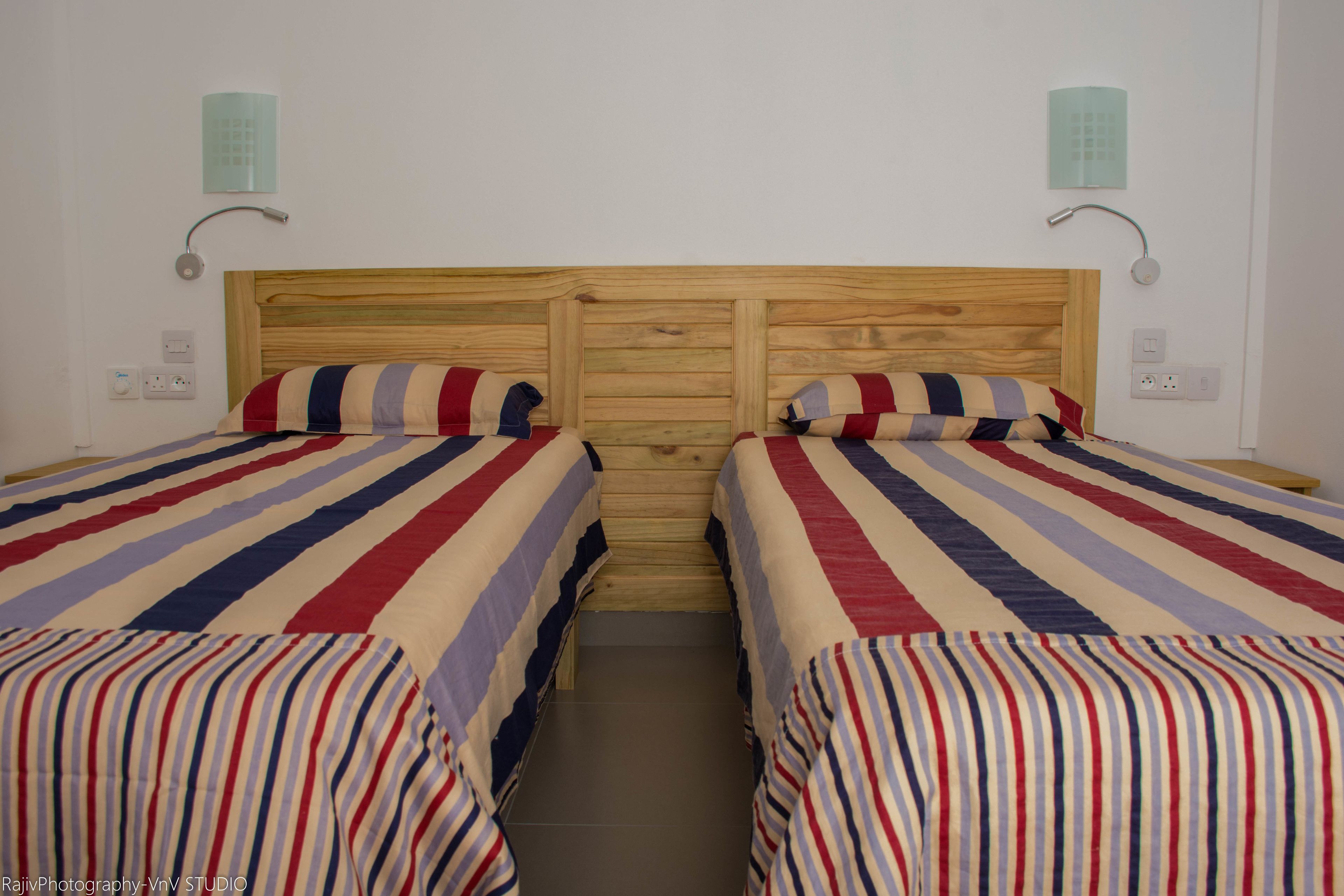 Une chambre avec deux lits, chacun doté de draps à rayures, de têtes de lit en bois et de lampes de chevet.