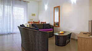 A furnished living room with wicker furniture, a glass coffee table, and a flat-screen TV. - Villa Alexis Self-Catering (Trou aux Biches)