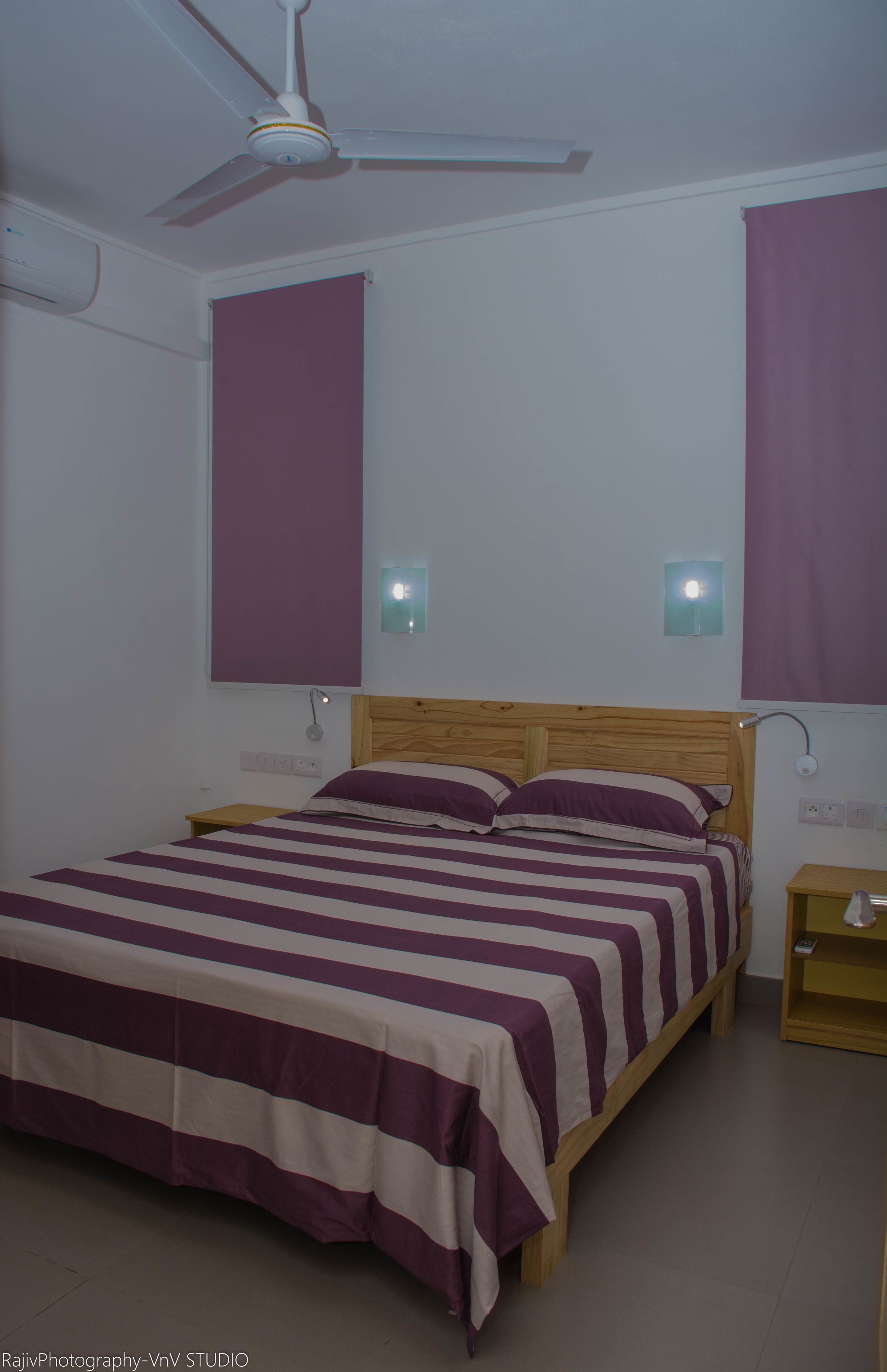 A bedroom with a bed, a ceiling fan, and two wall-mounted lights.