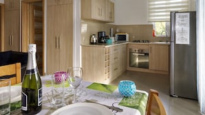 A modern kitchen with wooden cabinets, a stainless steel refrigerator, and a dining area with a table set for two. - Villa Alexis Self-Catering (Trou aux Biches)