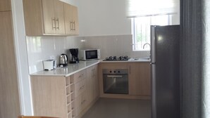 A compact kitchen with wooden cabinets, a microwave, a toaster, a coffee maker, a gas stove, and a dishwasher. - Villa Alexis Self-Catering (Trou aux Biches)