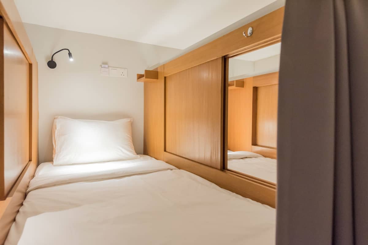 Una cama individual con cabecera de madera, una lámpara de noche y un espejo.