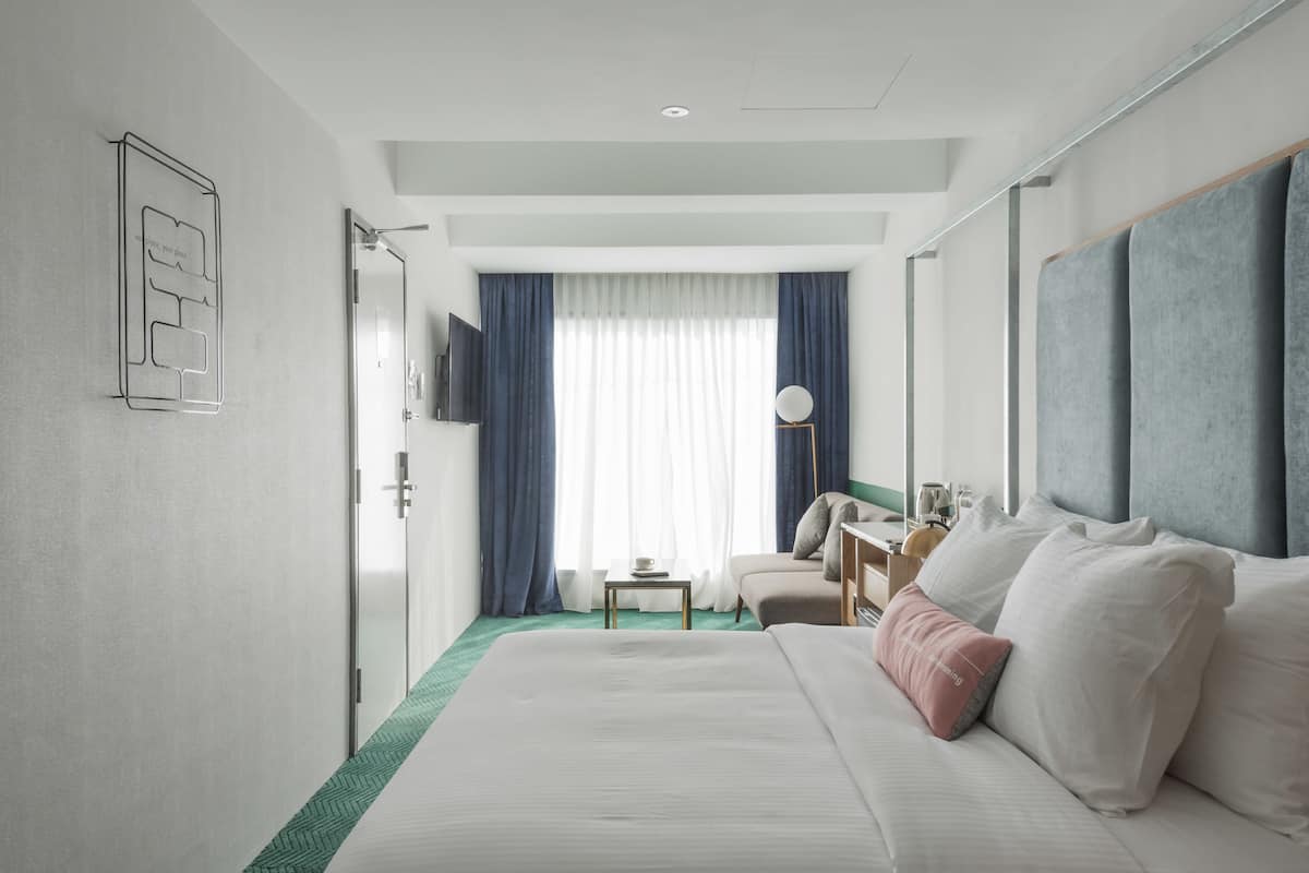 Habitación de hotel con una cama grande, un escritorio, una silla, un televisor y una ventana con cortinas.