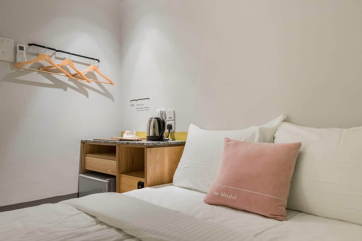 Habitación de hotel ordenada con una cama, un escritorio con hervidor y un tendedero en la pared.