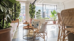 Un intérieur moderne avec des meubles en osier, des plantes en pot et de grandes fenêtres offrant une vue sur la ville.