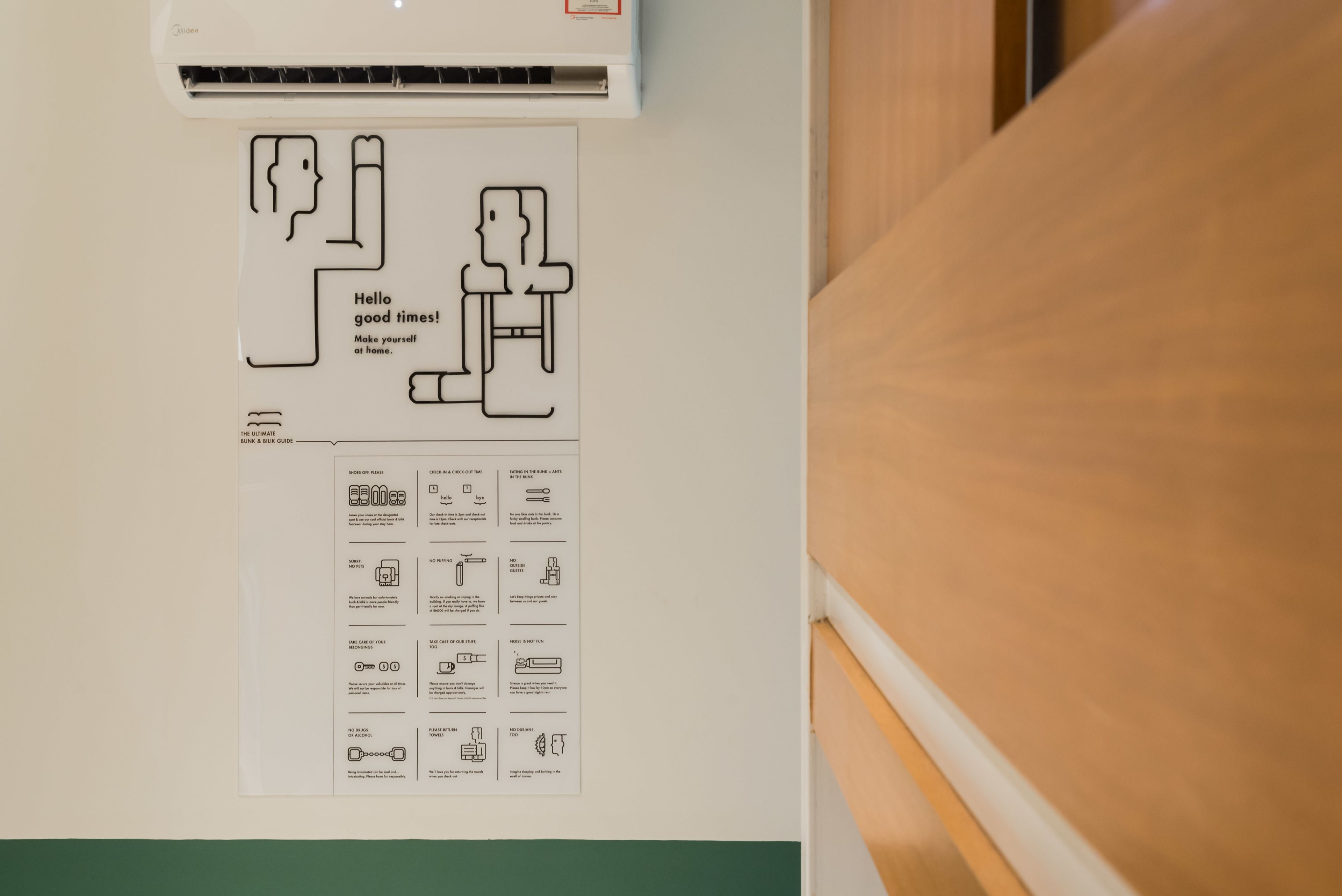 Un mur sur lequel est fixé un tableau blanc où figure un schéma et des instructions écrites, un appareil de climatisation blanc placé au-dessus, et une table en bois sur la droite.