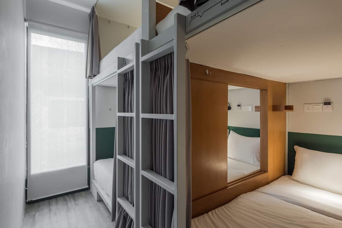Una habitación de hotel con literas, un ventanal con cortinas, un cabecero de madera y un espejo.