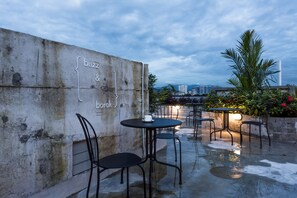 Un patio al aire libre con mesas y sillas, un muro de concreto con texto y un paisaje urbano de fondo.