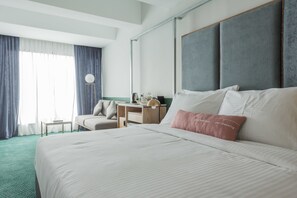 Ein Hotelzimmer mit einem großen Bett, einem Schreibtisch, einem Stuhl und Blick ins Freie.