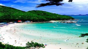 Una spiaggia con acque cristalline turchesi, sabbia bianca e colline verdeggianti sullo sfondo.