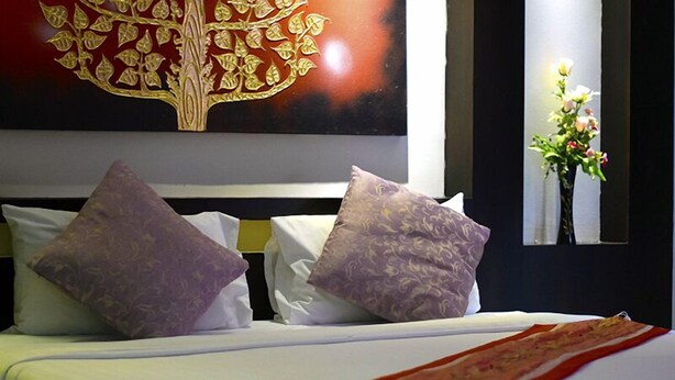 Un letto rifatto con copriletto rosso e bianco, due cuscini decorati e un grande elemento decorativo sopra il letto.
