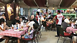 Un ristorante con tovaglie a quadri bianche e rosse, clienti seduti ai tavoli e un cameriere in divisa bianca e rossa.