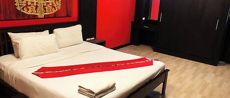 A neatly made bed with white linens, a red decorative cloth, and a folded towel on the side.