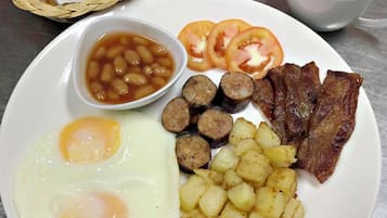 A breakfast plate with eggs, sausages, bacon, potatoes, beans, tomatoes, toast, juice, and coffee.