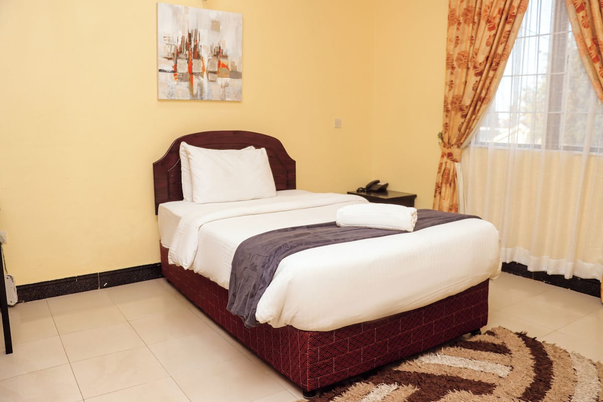 A neatly made bed with a patterned bedspread and pillows, a bedside table with a phone, and a painting on the wall.