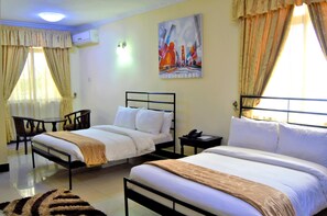 A hotel room with two beds, a desk, and a chair. There is a painting on the wall and an air conditioning unit. - M Hotel Mbezi (Dar es Salaam)
