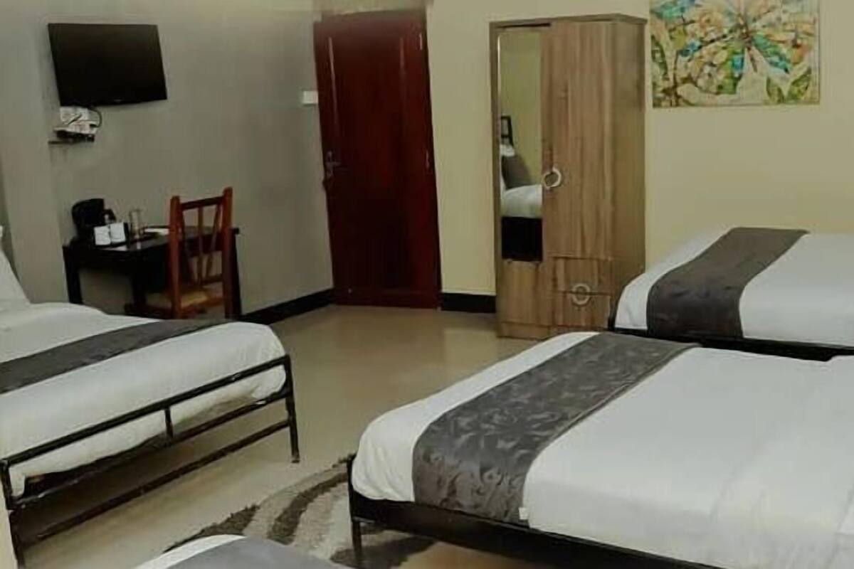 A hotel room with two beds, a desk, a chair, a wardrobe, and a TV on the wall.