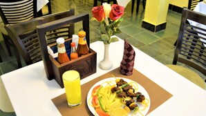 A dining table with a plate of food, a bottle of sauce, a vase with flowers, and a glass of juice. - M Hotel Mbezi (Dar es Salaam)