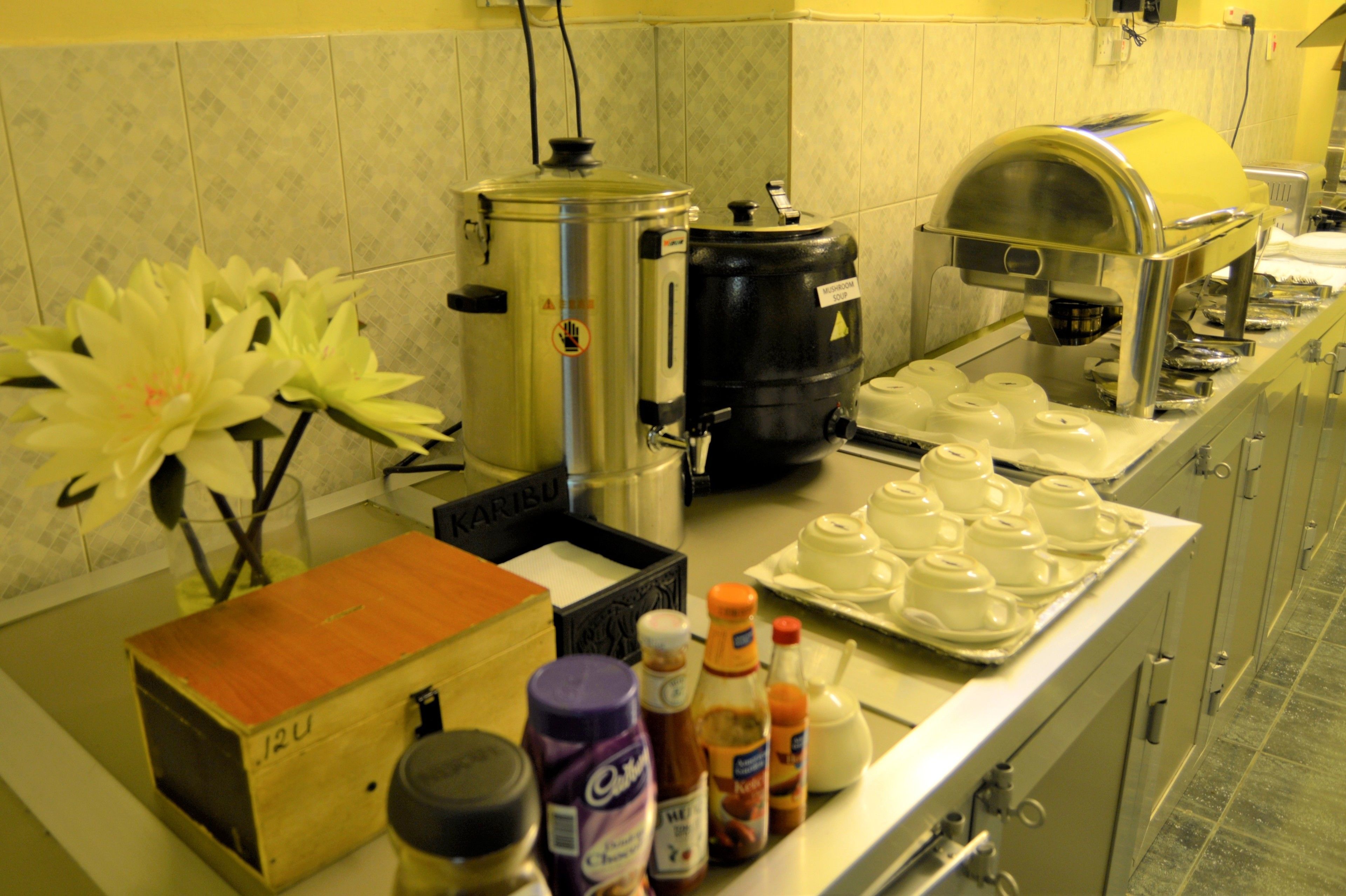 A kitchen with a coffee station, including a coffee machine, a large black container, and a tray of white cups.