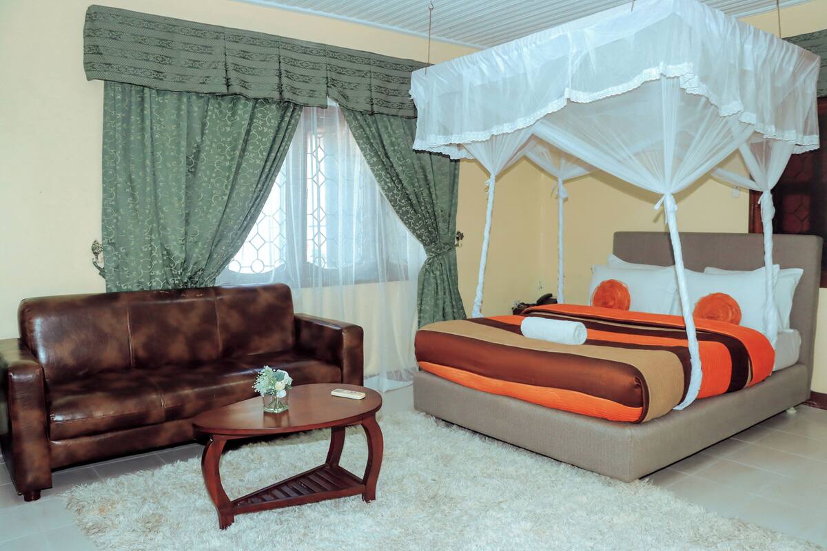 A bedroom with a bed, a sofa, a small table, and a window with curtains.