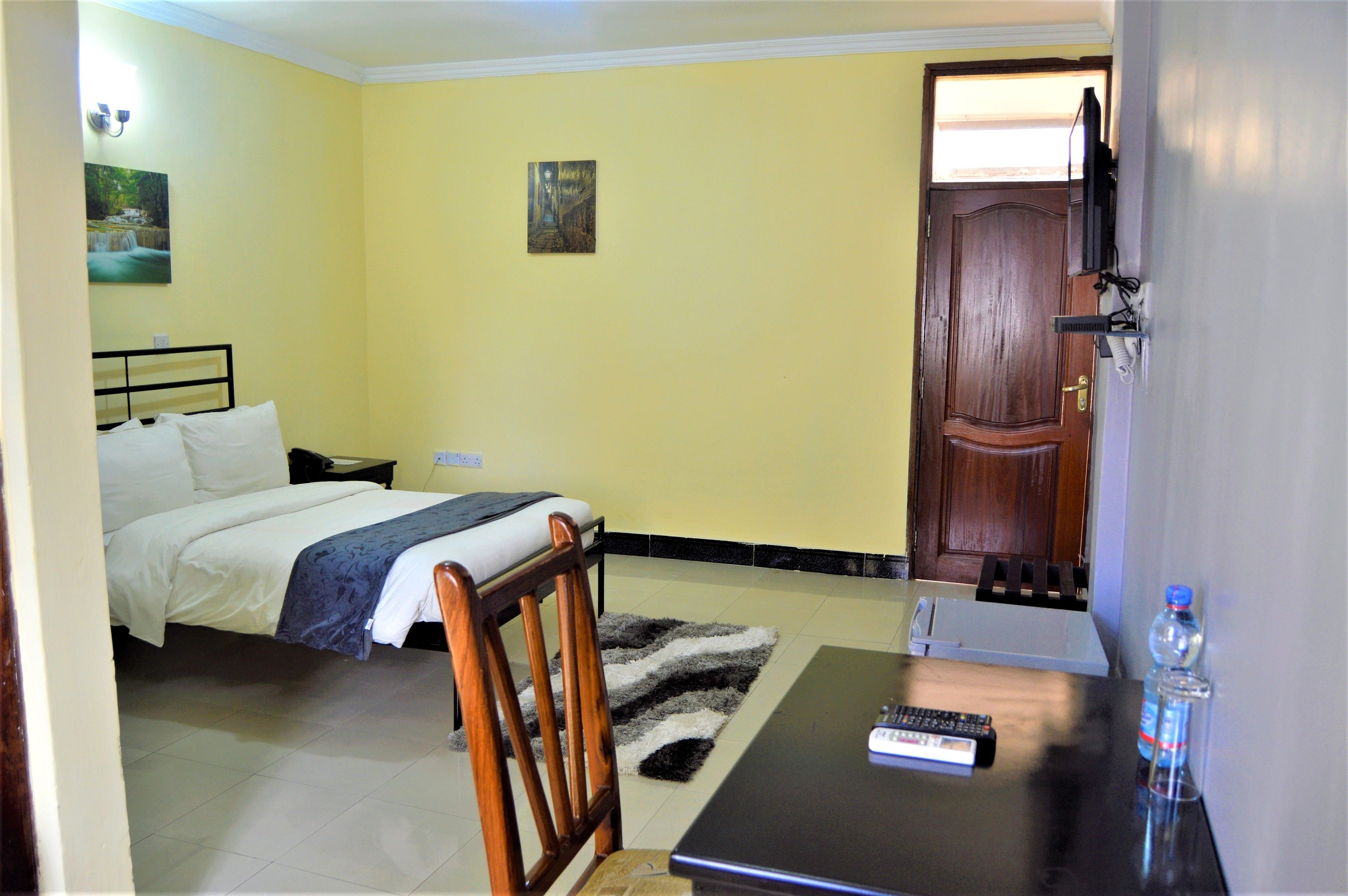 A hotel room with a bed, a chair, a desk, a television, and a door.