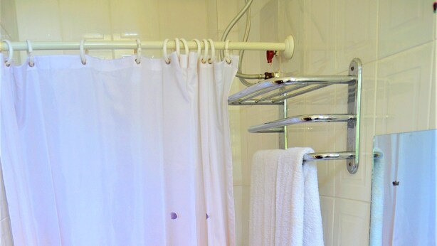 A bathroom with a shower curtain, a sink, a mirror, and a towel rack. - M Hotel Mbezi (Dar es Salaam)