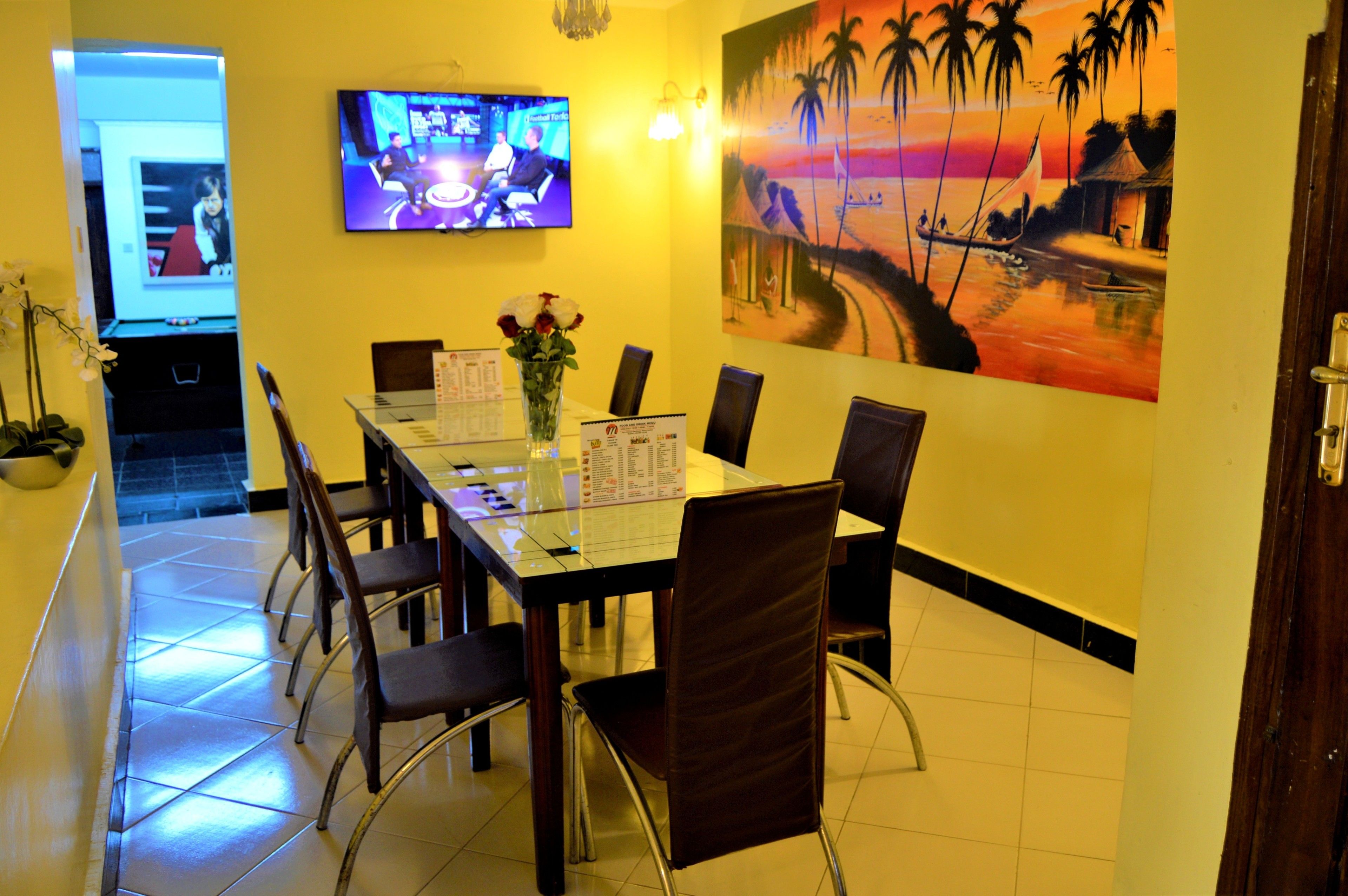 A conference room with a glass table, chairs, a TV on the wall, and a painting of a sunset scene.