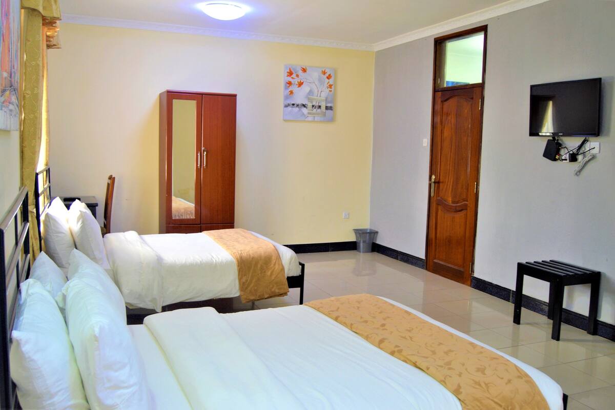 A hotel room with two beds, a television, a mirror, and a wooden wardrobe.