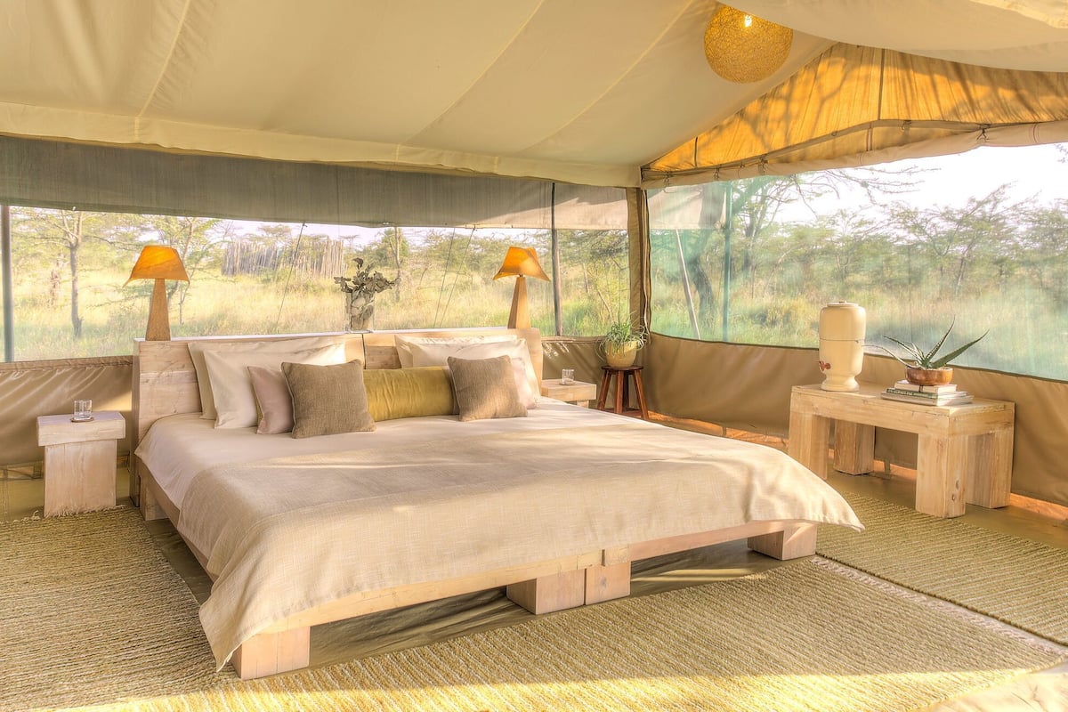 A spacious bedroom with a large bed, two bedside lamps, a wooden nightstand, and a small table with a vase and books.