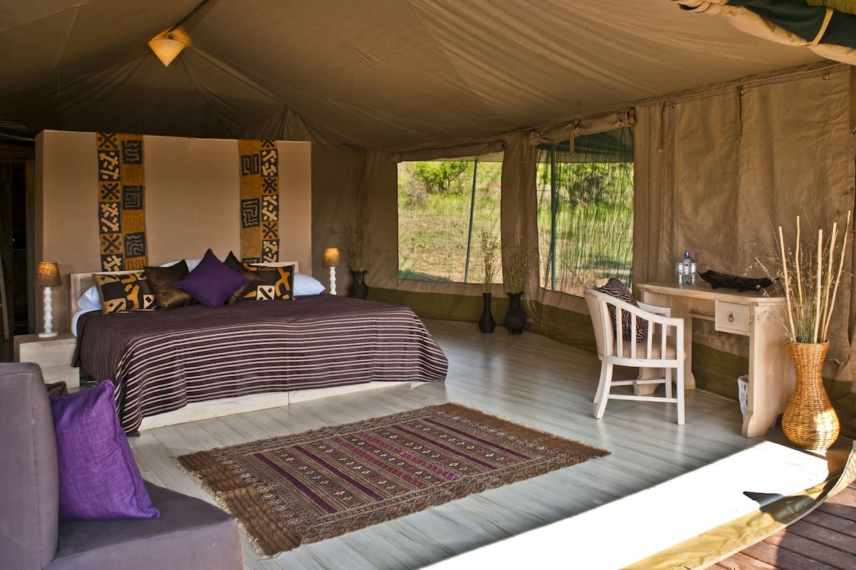 A tented room with a bed, a desk, a chair, and a view of the outdoors.
