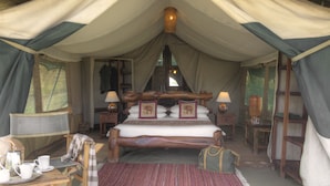 Habitación tipo alojamiento con carpa, una cama grande, dos mesitas de noche con lámparas, un cabecero de madera y vistas a través de la ventana.