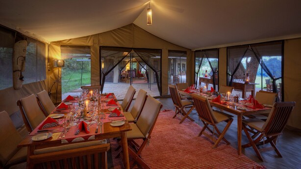 Un comedor con toldo, mesas dispuestas para una comida, sillas y vistas al exterior.