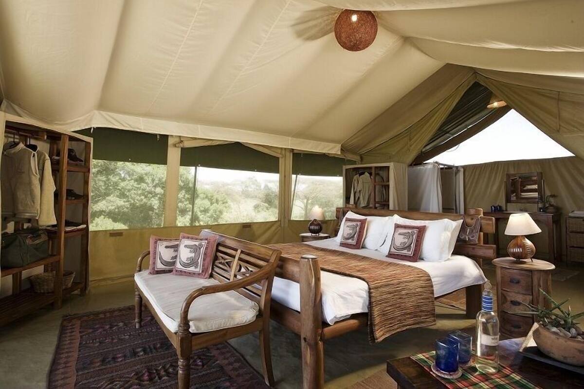 A tented accommodation with a bed, wooden furniture, a table, and a view of the outdoors.