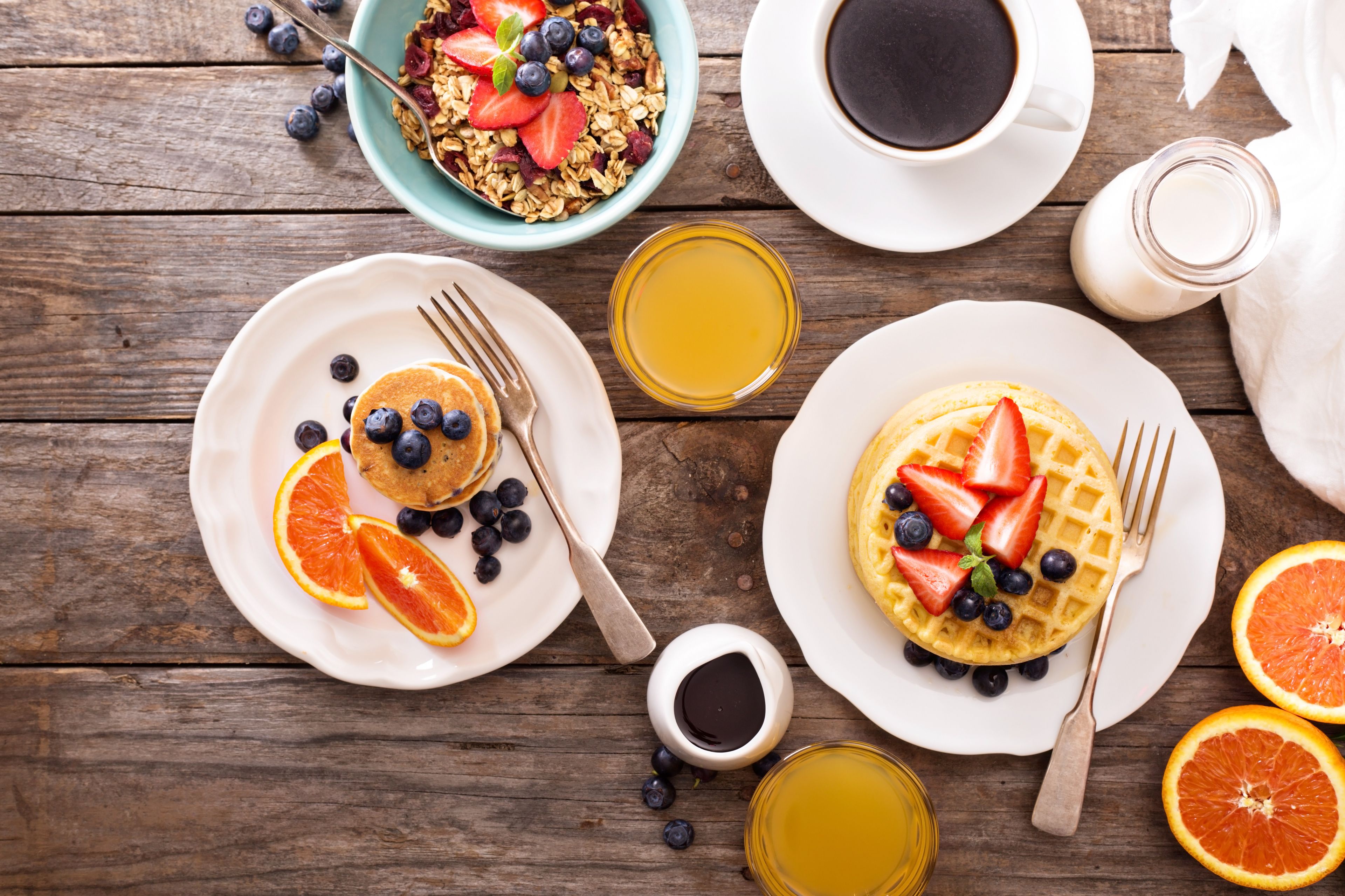 A breakfast setting with pancakes, waffles, and fruit on plates, accompanied by coffee and juice.